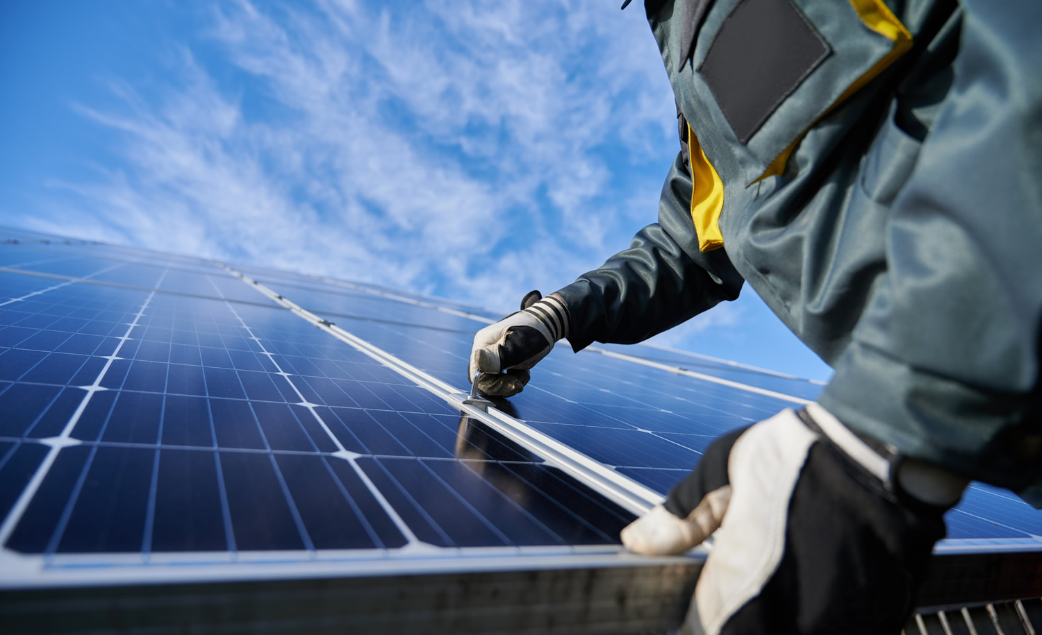 Close up of man technician in work gloves installing stand-alone photovoltaic solar panel system under beautiful blue sky with clouds. Concept of alternative energy and power sustainable resources 